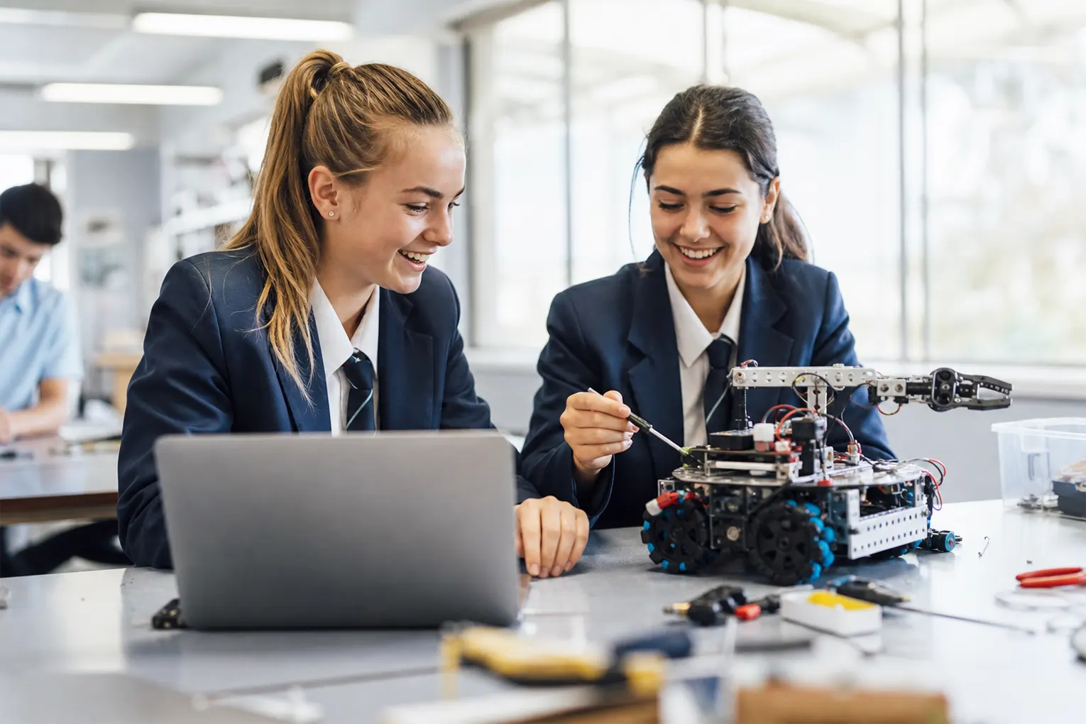 Two Australian teenage girls in school uniforms collaborating on a robotics project in a Makerspace